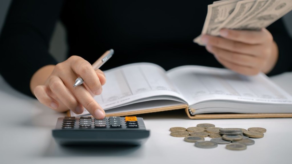 Woman using calculator with pen in her hand and hold dollar bill for calculating financial expense at home office, financial accounting calculate money payments manage expenses.