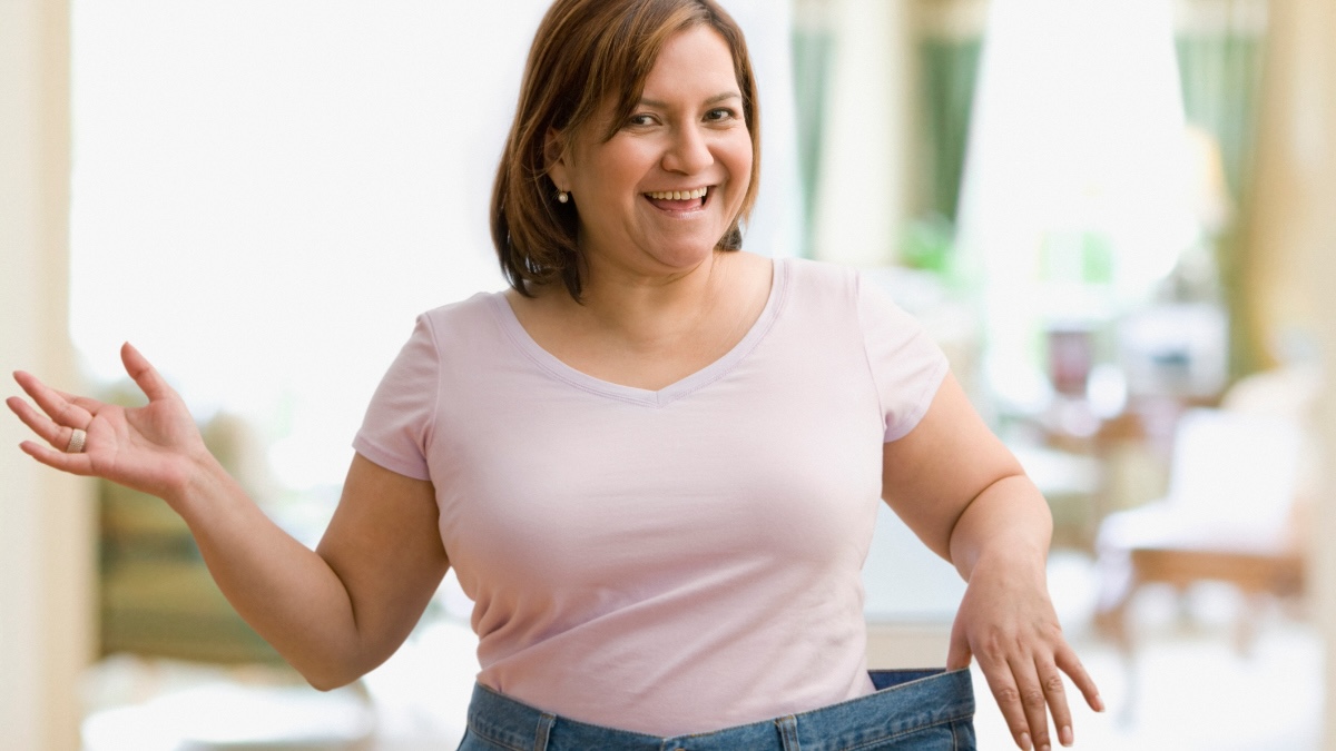 Woman smiling while holding the loose waistband of her jeans after weight loss