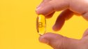 Close-up of a hand holding a B12 capsule against a yellow background