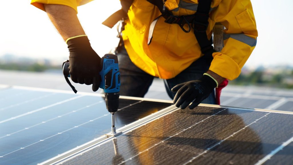 Male technician in yellowsuit installing photovoltaic blue solar modules with screw. Man electrician panel sun sustainable resources renewable energy source alternative innovation