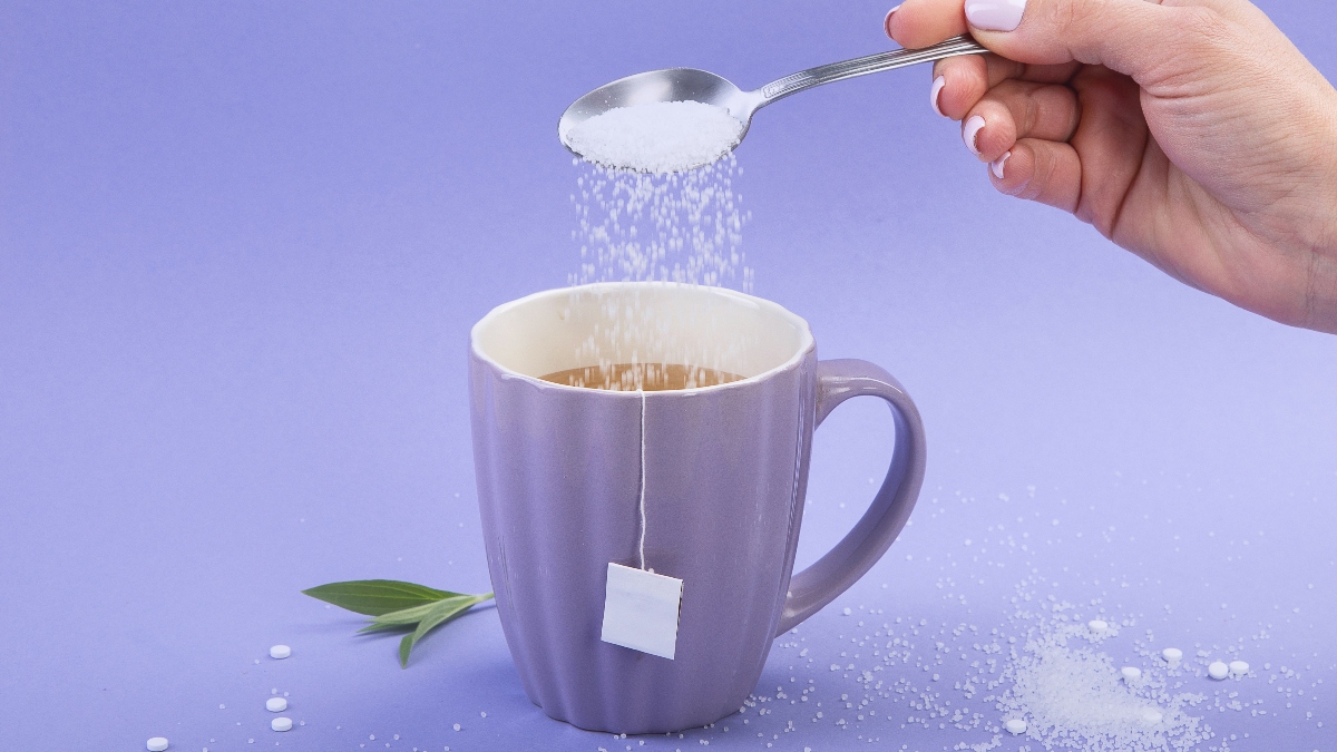 hand pouring sugar into cup of tea