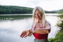 Portrait of beautiful woman standing on lake shore after run in nature, checking her performance on smartwatch.