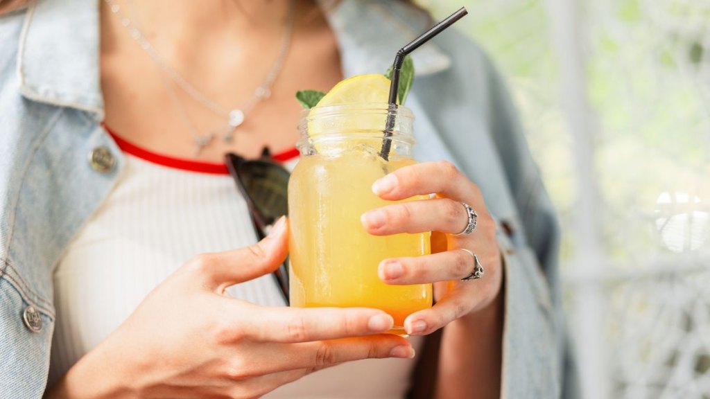 Freshly squeezed lemon-orange juice with ice with mint leaves in female hands. Woman holding vintage cup with citrus cool lemonade drink. Close-up.