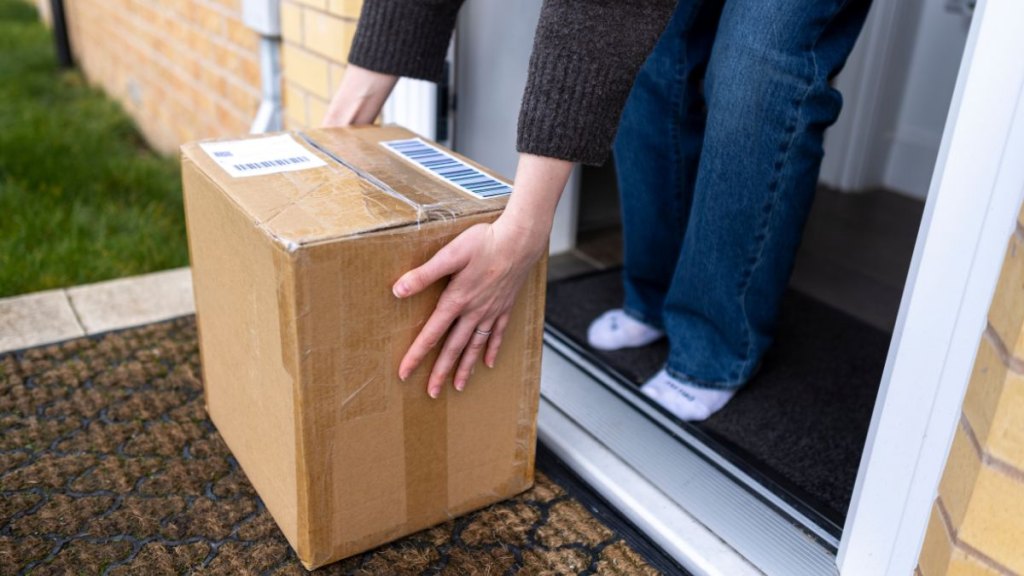 A medium unrecognisable shot of a woman bending down to pick up a package left at her doorstep. The scene highlights the convenience of home delivery, online shopping, and contactless drop-offs. Videos are available similar to this scenario.