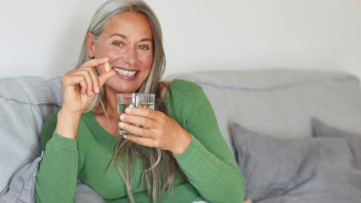 Smiling woman with diabetes taking a supplement with a glass of water