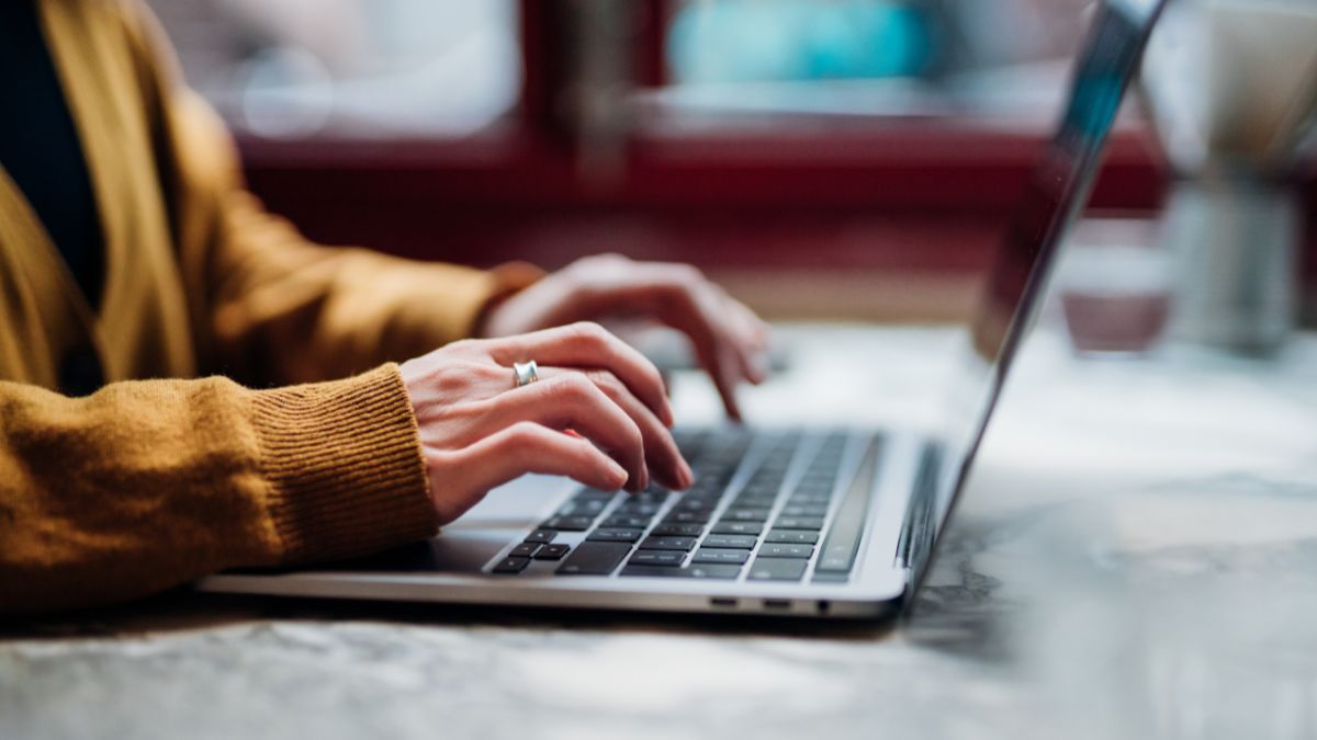 Side view of female hand typing on laptop keyboard. Freelancer working with laptop at cafe. Technology and flexible working.