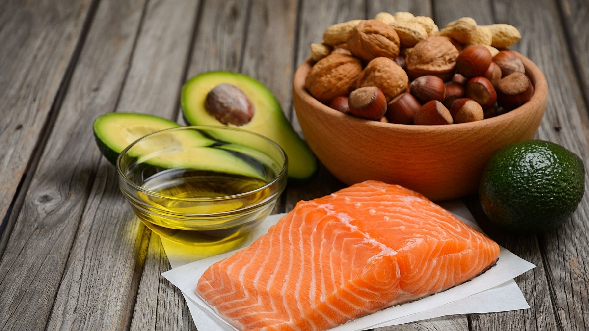 A collection of healthy fats for blood sugar, including fatty fish, olive oil, avocado and nuts on a table