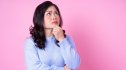 A woman with her hand on her chin looking up while thinking and dealing with memory loss against a pink background
