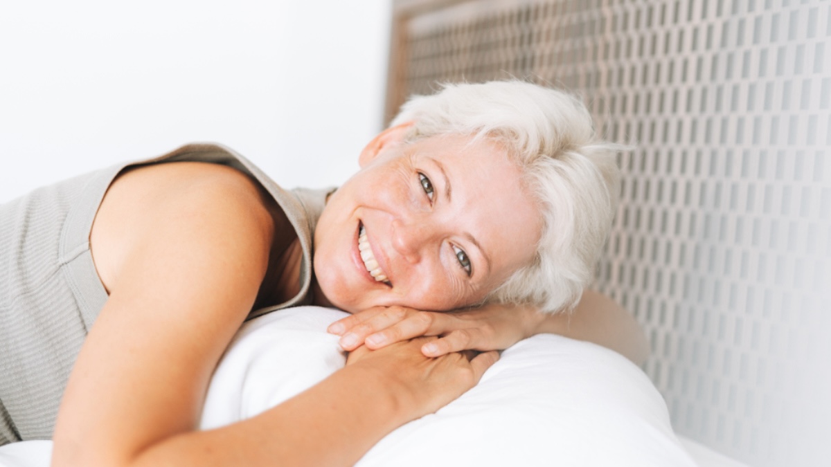 middle-aged woman smiles while lying down in bed for sleep