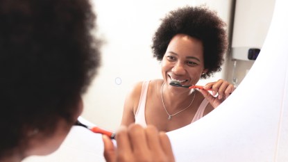 woman brushing her teeth and looking in mirror
