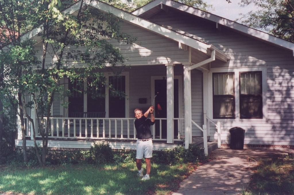 Ex-child actor Keith Thibodeaux, exec. dir. of the Ballet Magnificat, swinging a golf club on front lawn of his modest single-story home.