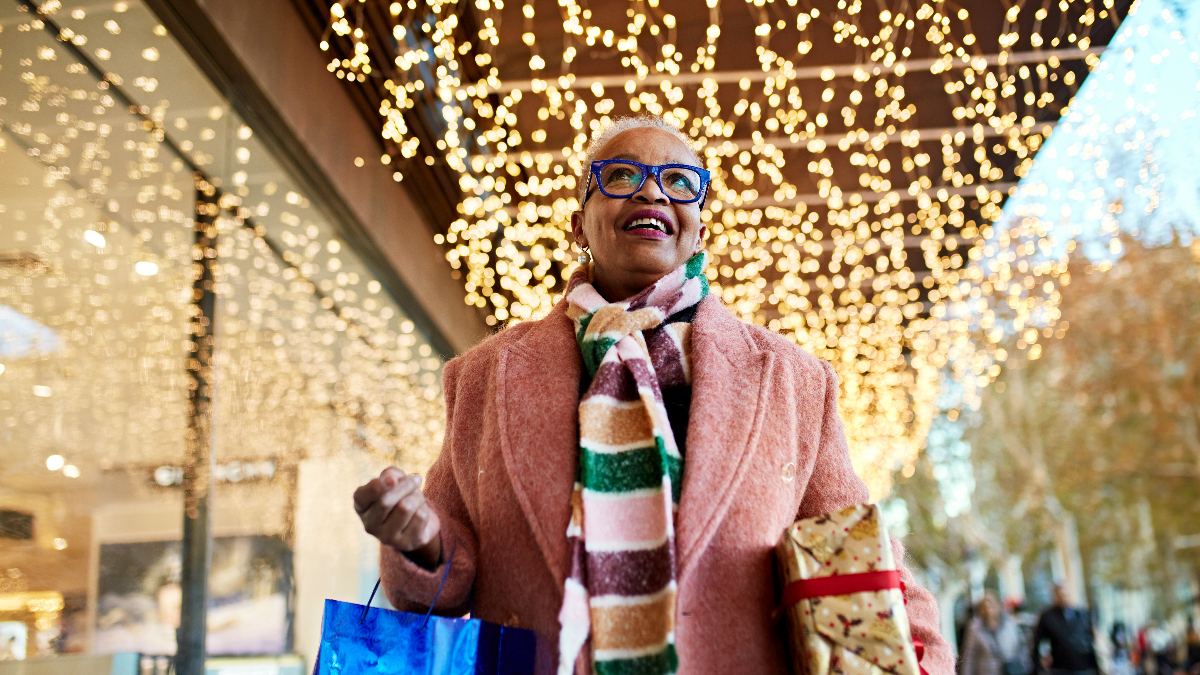 middle-aged woman happily carries shopping bags as she shops for holiday gifts