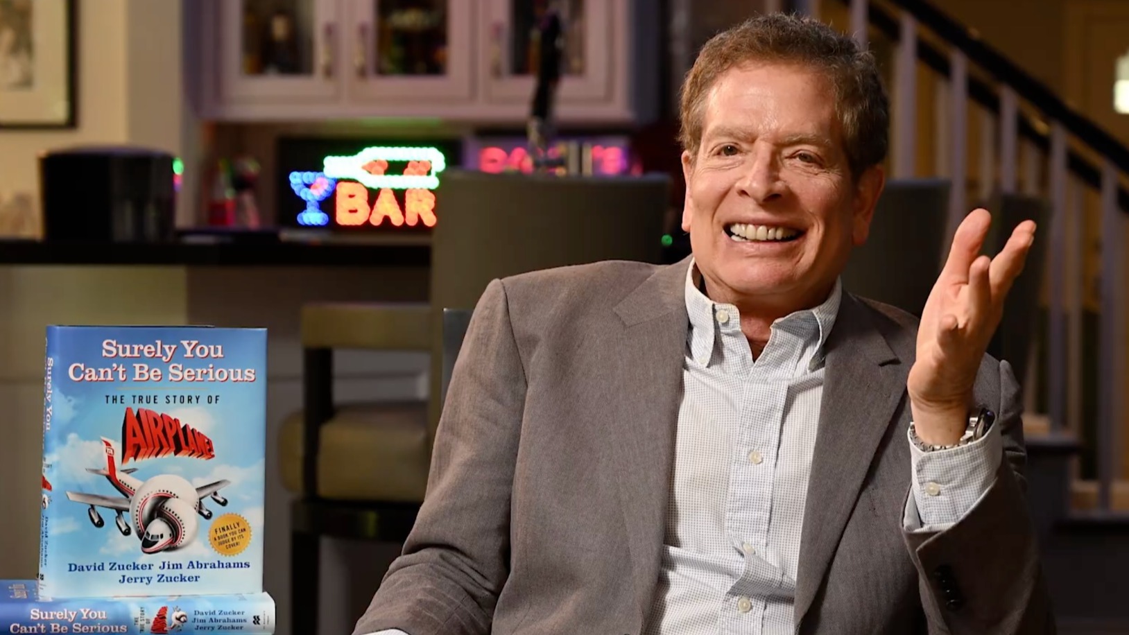 David Zucker poses with a copy of his 2023 book 'Surely You Can't Be Serious: The True Story of Airplane!' cowritten with his collaborators Jerry Zucker and Jim Abrahams