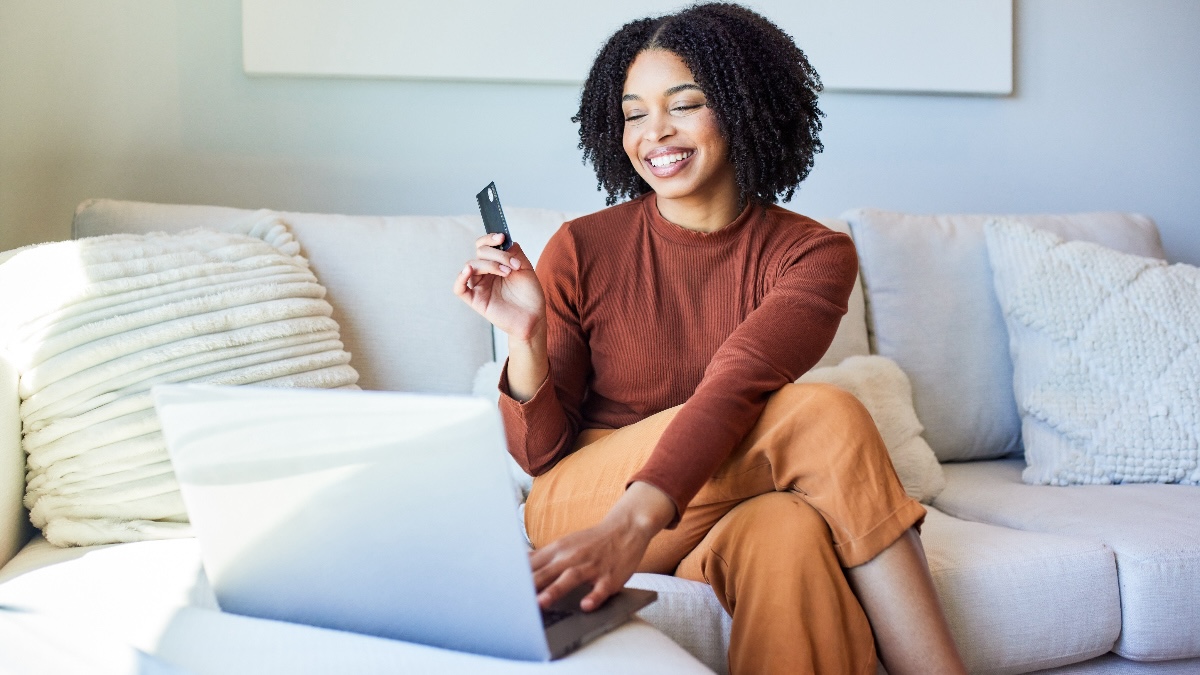 young woman happily holds credit card in one hand and types on her laptop with the other, as she hunts down Cyber Monday deals