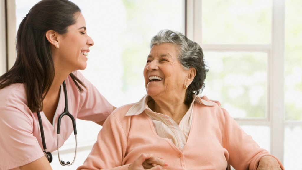 Female nurse smiling and talking with an elderly woman in a wheelchair.