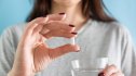 Close-up of a woman holding a statin pill and a glass of water