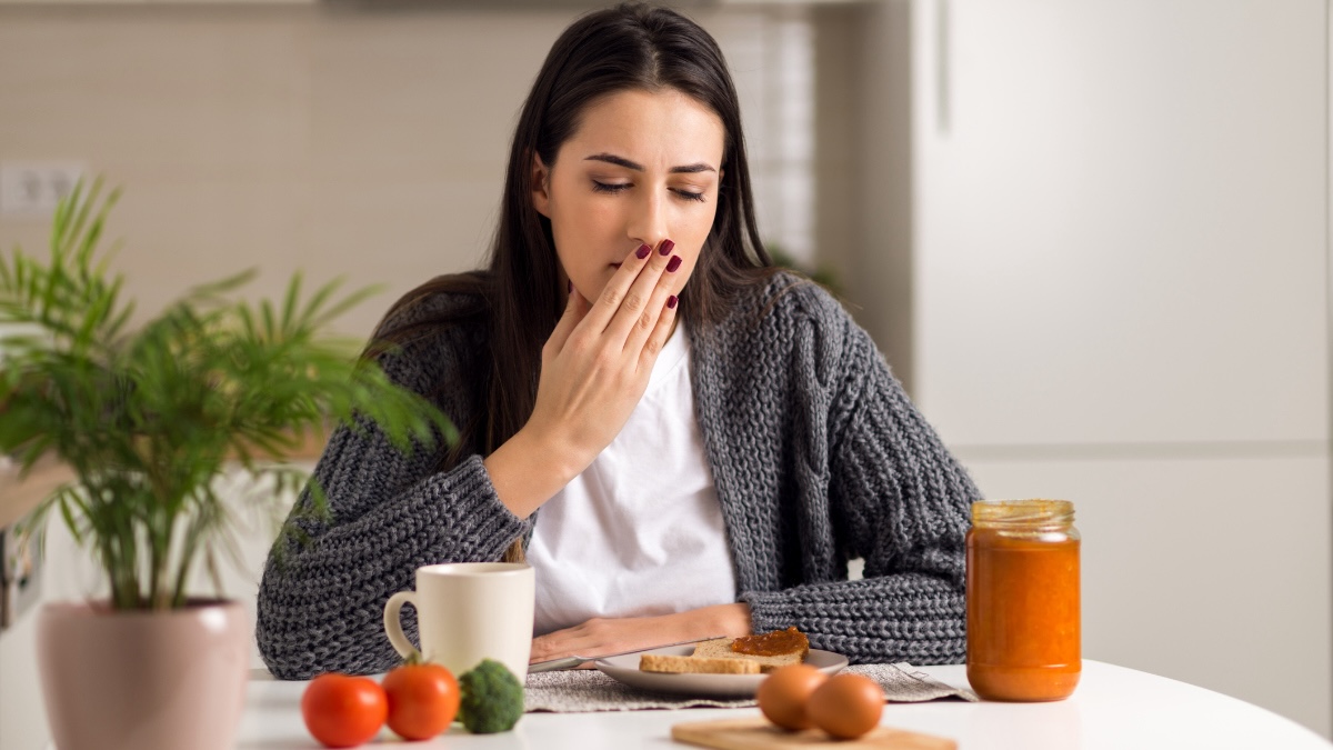 Nauseous woman with her hand over her mouth looking at her breakfast in the morning