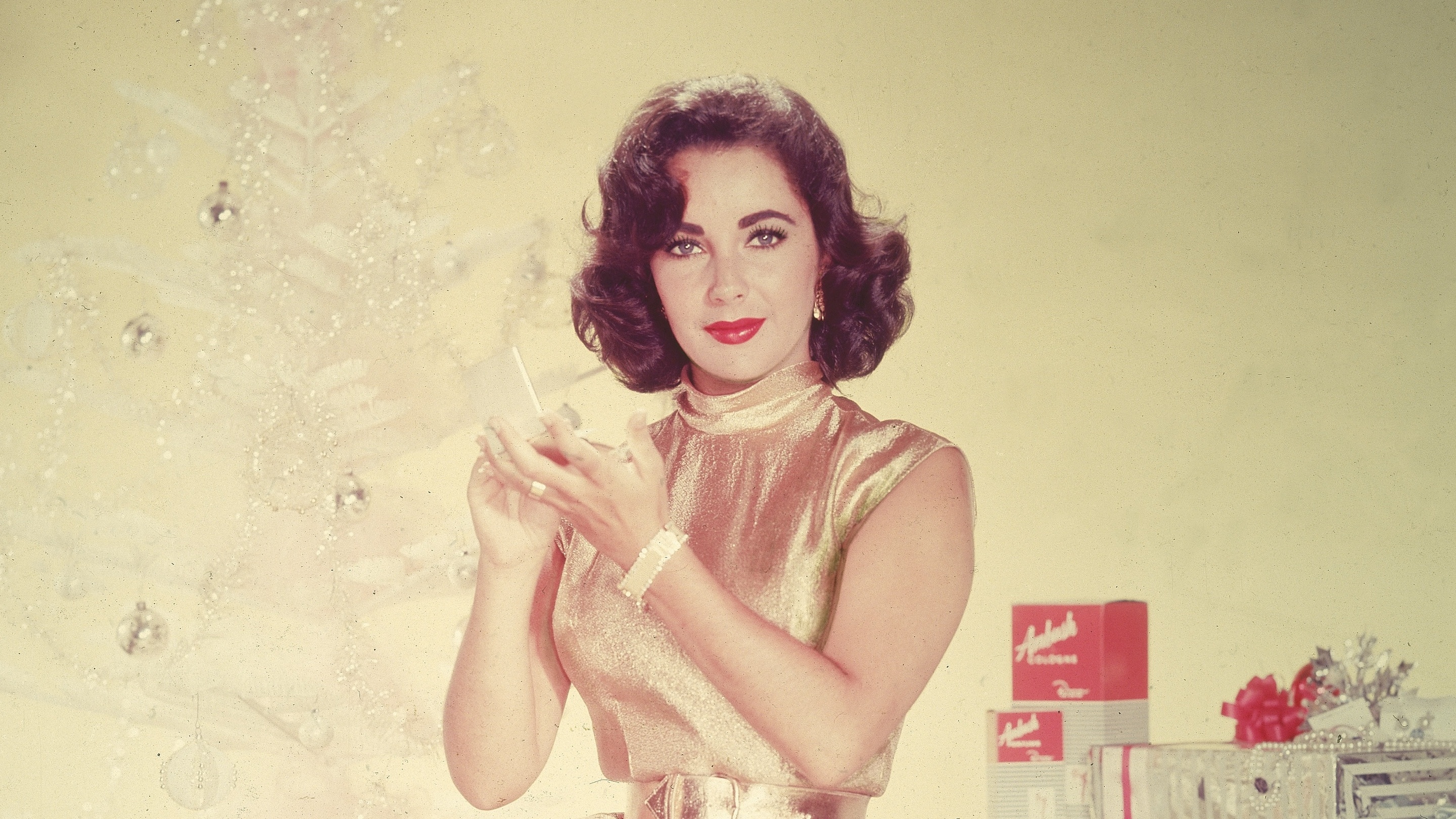 Elizabeth Taylor poses with a Christmas tree and presents in 1955