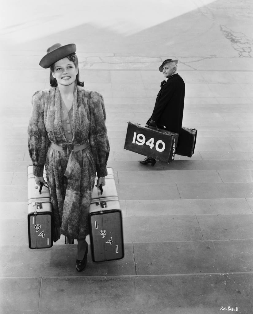 1941: A young Rita Hayworth sees in the New Year with a pair of '1941' suitcases as she passes writer Quentin Crisp carrying a pair of '1940' suitcases on the way out. 