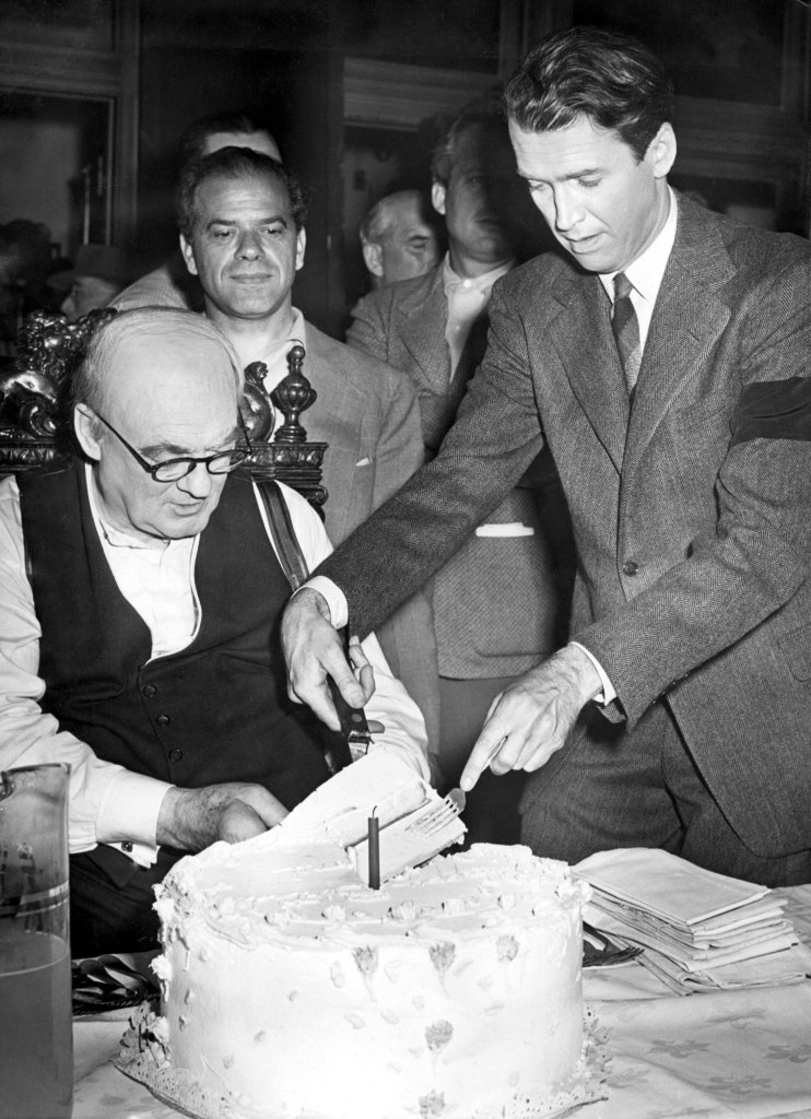 James Stewart and Frank Capra present Lionel Barrymore with birthday cake on the set of It's a Wonderful Life