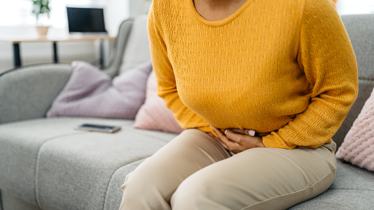 woman sitting on sofa puts her hands on her stomach, as if she is experiencing nausea or indigestion from antibiotics