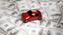 photo of small, red toy car placed on a "road" of 100-dollar bills