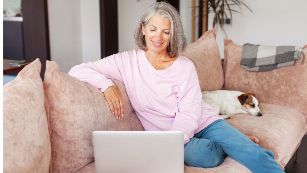 Mature woman using wireless laptop apps browsing internet sit on sofa