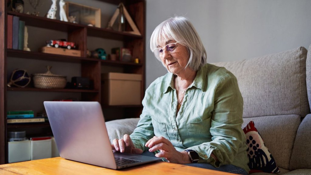 Senior woman using a laptop sitting on the sofa in a house
