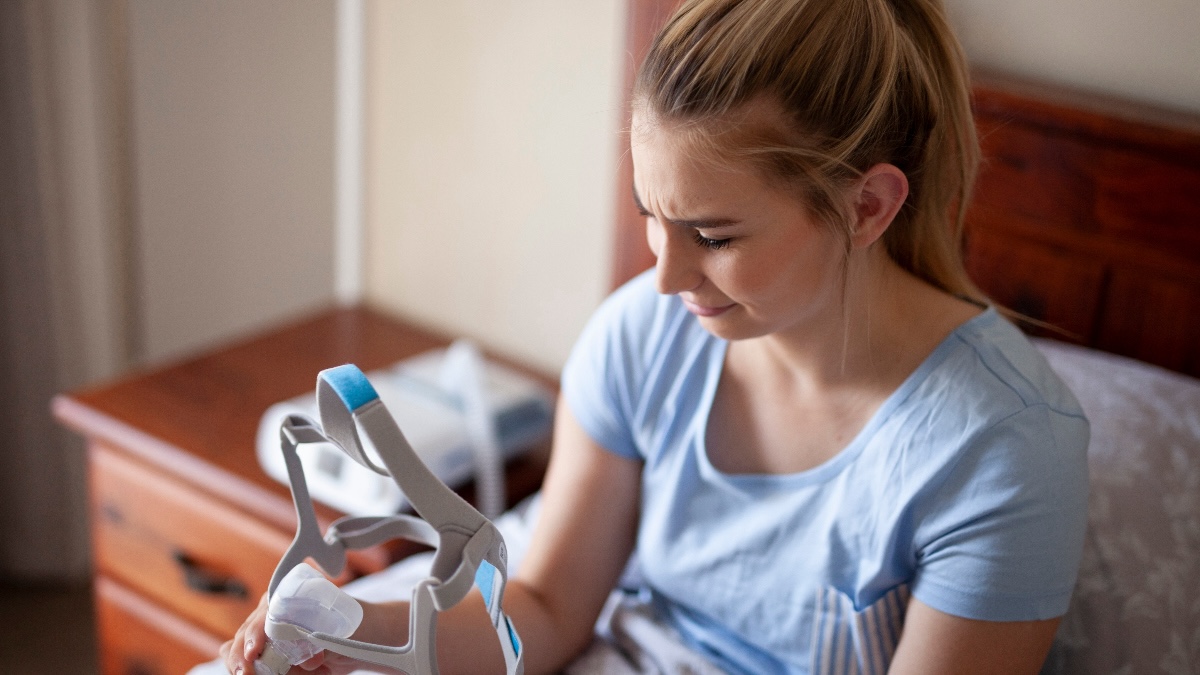 A woman looks quizzically at her CPAP machine as she struggles to use it