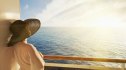 woman in broad sun hat looks out at see from the deck of a cruise ship