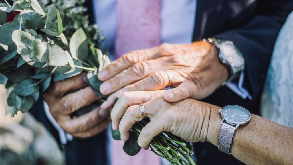 Cropped image of newlywed couple showing rings while holding bouquet during wedding ceremony