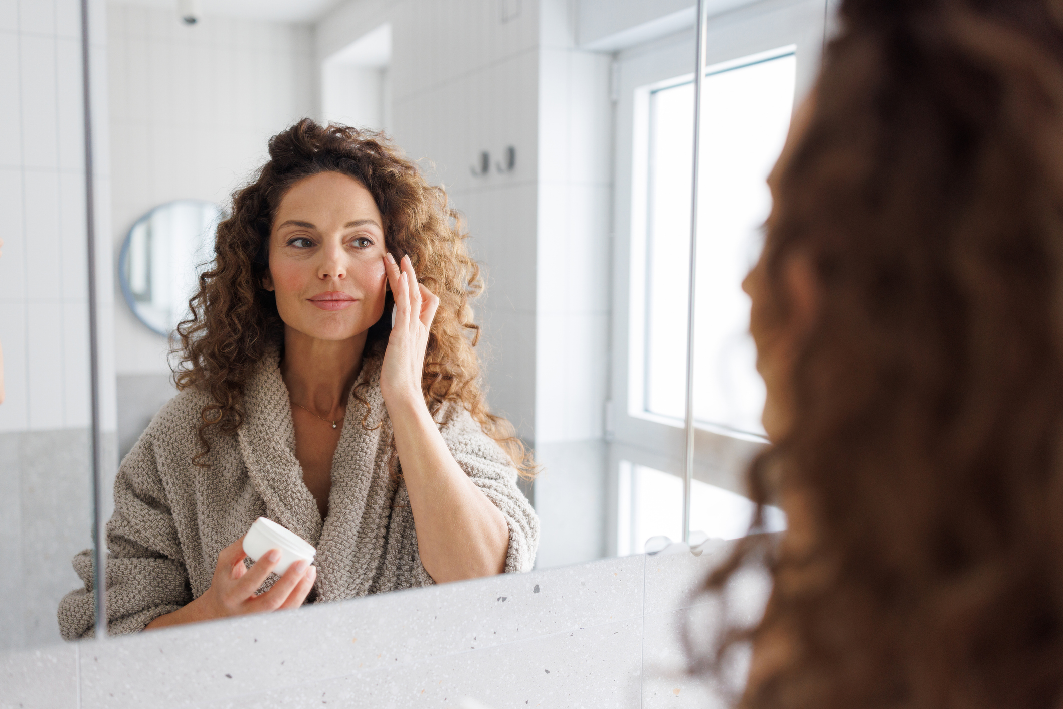 A mature woman applying skincare to her face.