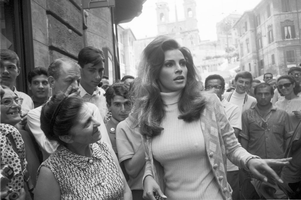 View of Raquel Welch surrounded by onlookers, as she walks along a street, Rome, Italy, July 1966. 