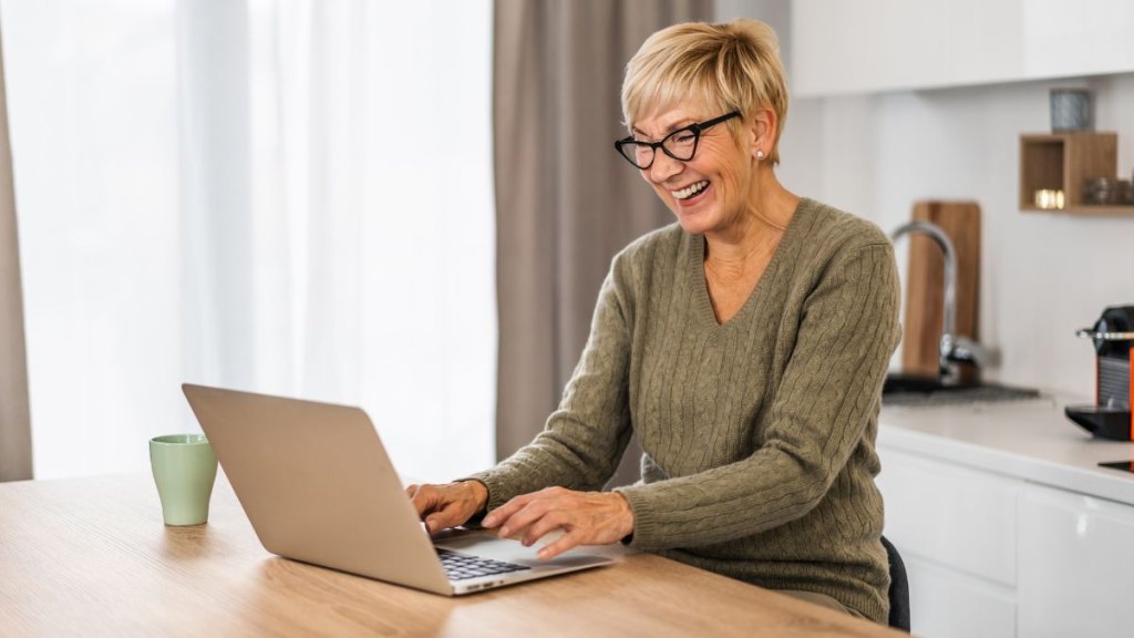 Senior woman smiling while working on laptop in kitchen