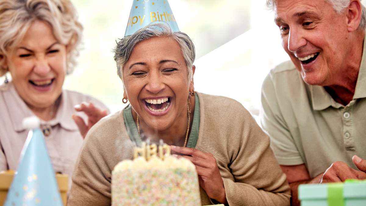 Mature woman surrounded by friends blows out the candles on her birthday cake after learning how to overcome aging anxiety