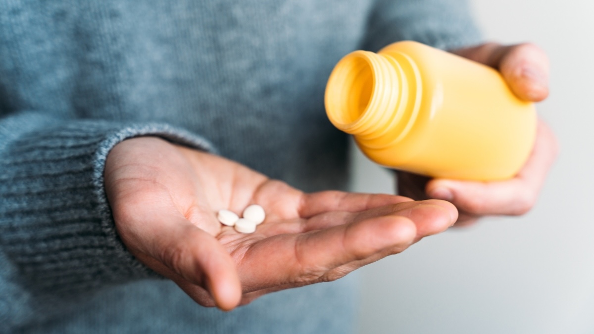 Close-up of a woman pouring out NSAIDs such as naproxen or ibuprofen from a pill bottle for pain relief