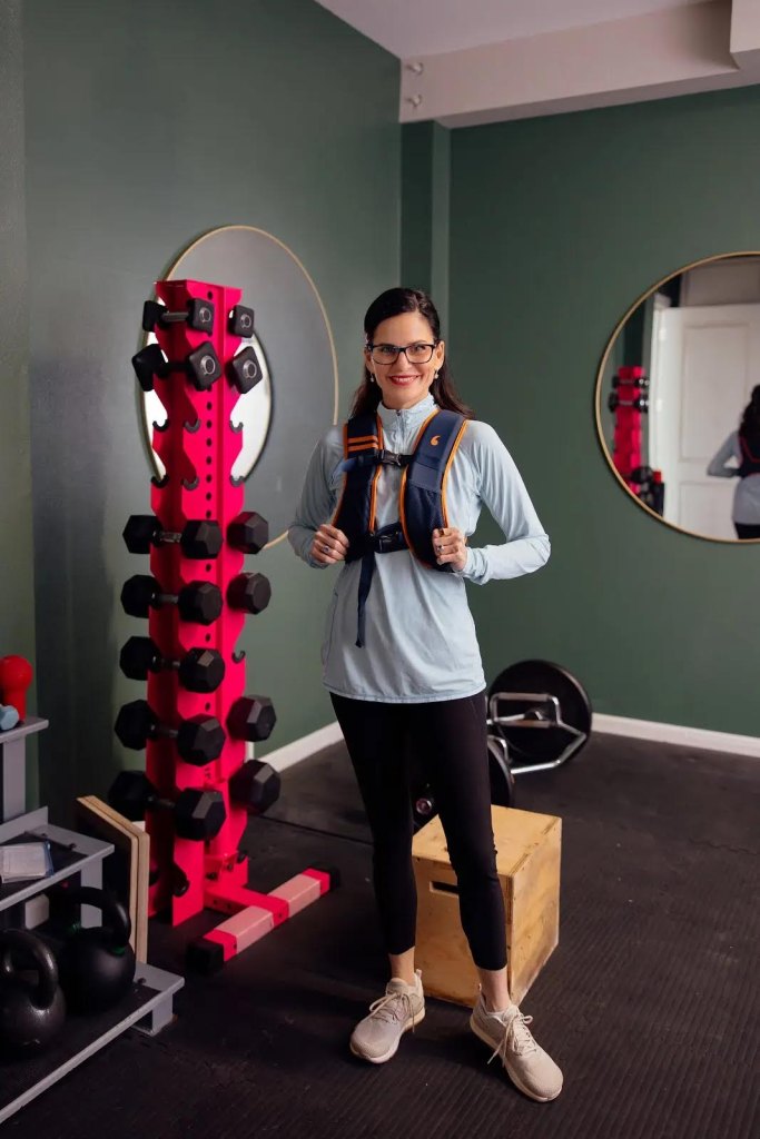 Mary Claire Haver wears a weighted vest while posing next to a weight rack