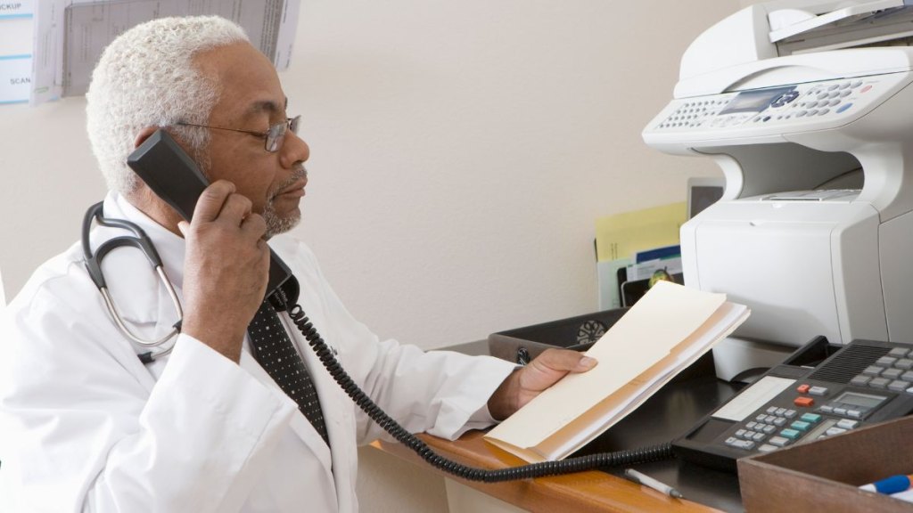 African American senior male doctor holding document while using phone