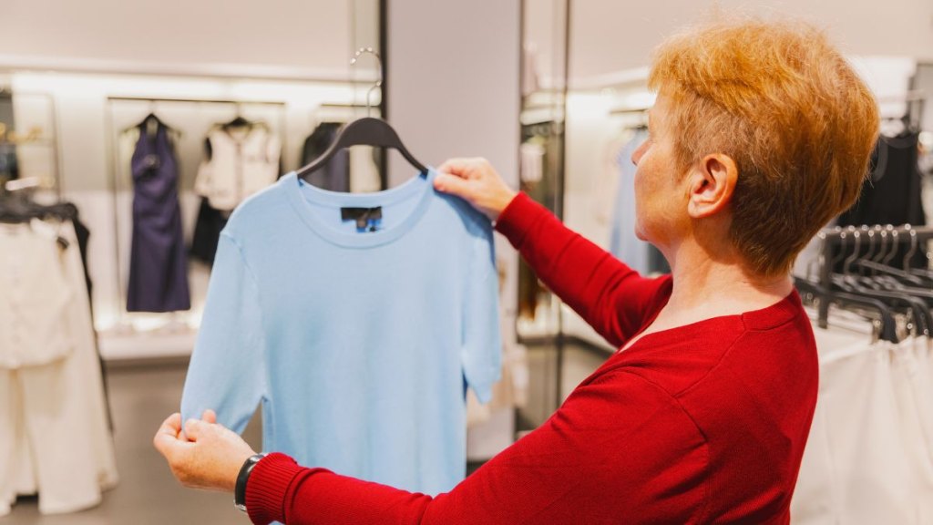 An elderly woman examines a sky blue T-shirt in a store