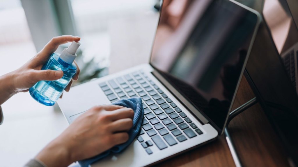 Cropped shot of a young woman cleaning the surface of laptop with cleaning spray and antistatic cloth at home