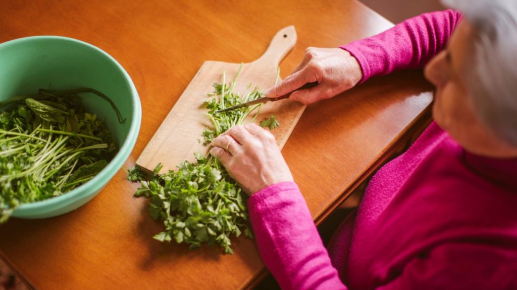 Elderly woman chopping fresh herbs at home kitchen table