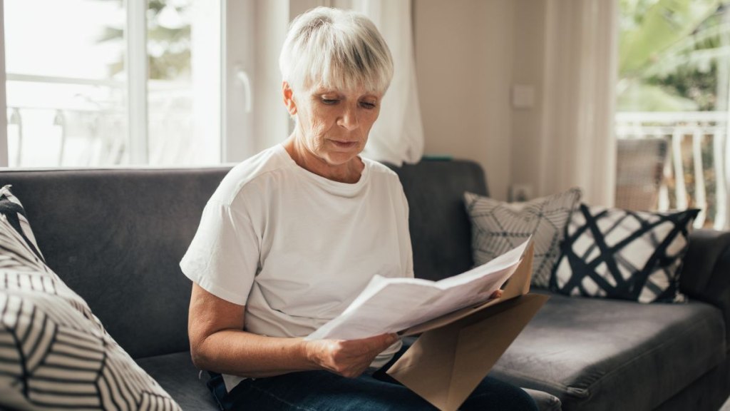 Grey-haired Senior Woman Reviewing Paper Financial Statements and Bills at home. Life on retirement