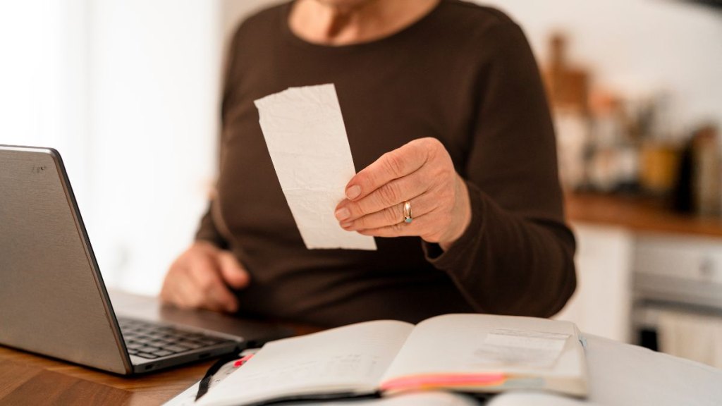 Senior woman doing taxes at home with laptop and receipts