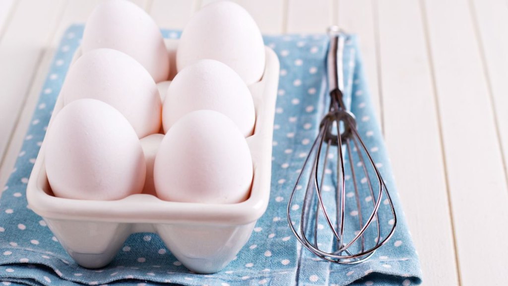 Six fresh eggs in egg holder with a whisk