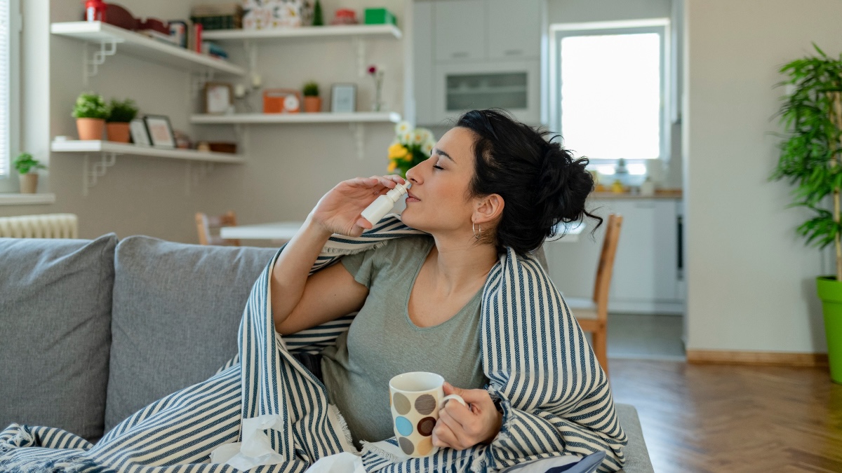 woman with high blood pressure and a stuffy nose uses a nasal decongestant while sitting on her couch