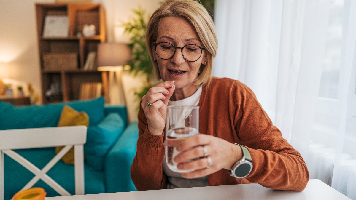 Woman takes a blood thinner pill, such as Eliquis or warfarin, with water