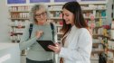 A pharmacist pointing to a tablet to share her insider secrets to a mature woman customer
