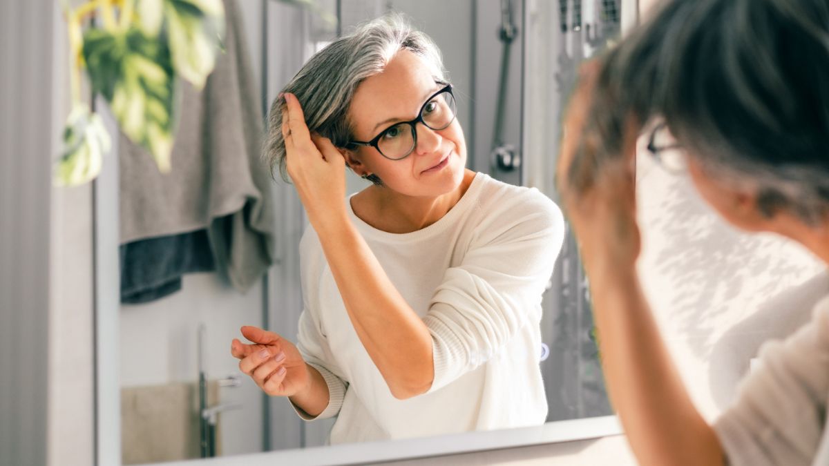 Mature woman styling hair after using red algae products while looking into the bathroom mirror