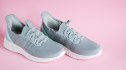A pair of grey slip-on shoes against a pink background