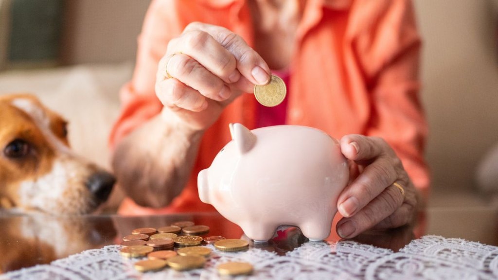 Senior woman saving money in piggy bank with dog